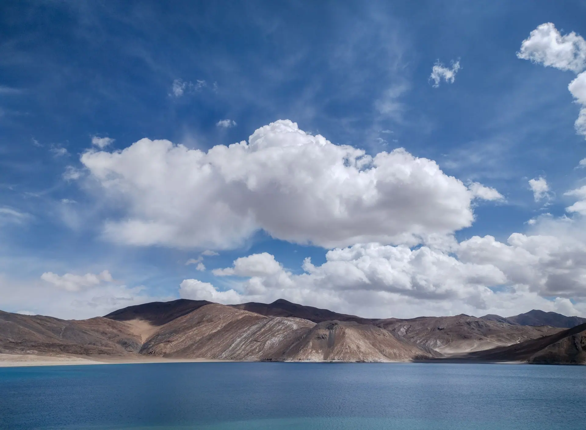 A breathtaking view of Pangong Lake's turquoise waters and dramatic clouds under a clear blue sky