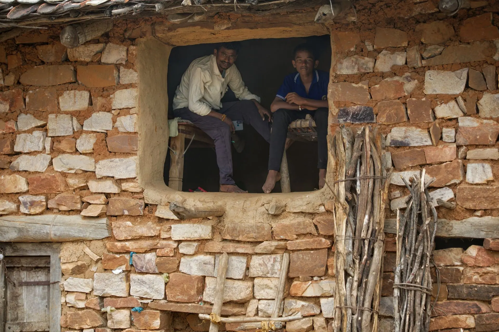 Two men sitting in a rustic stone house window in Chitrakoot, India, showcasing rural life