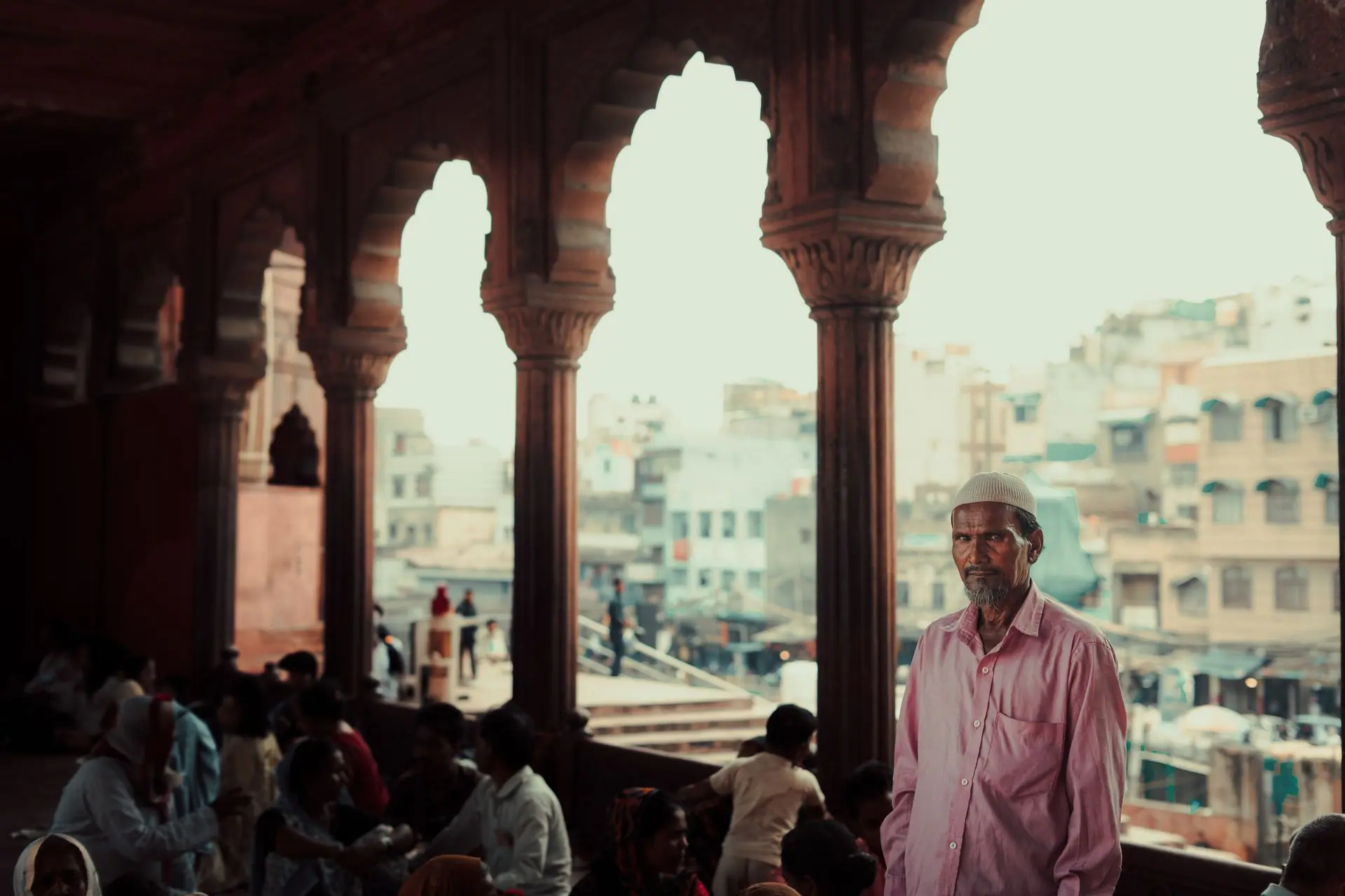 Elderly man stands in a historic mosque overlooking Old Delhi's vibrant streets