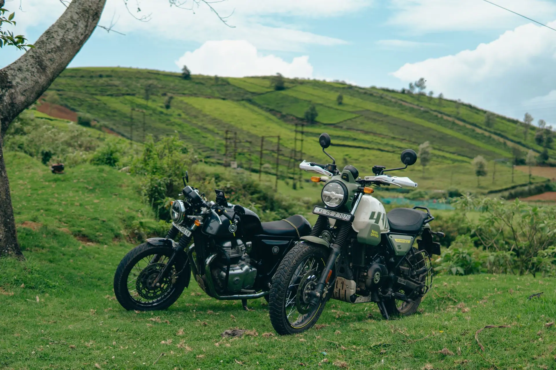 Two classic motorcycles parked on lush green hills of Ooty, Tamil Nadu, India with a scenic view of tea plantations