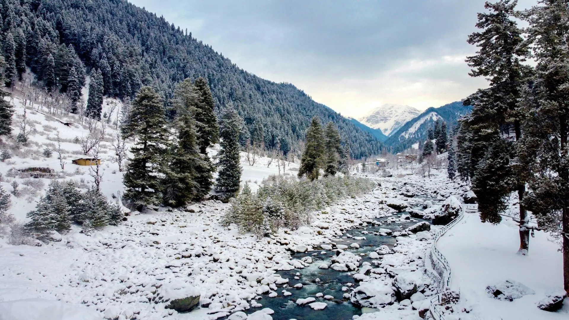 Scenic winter landscape in Pahalgam with snow-covered trees and mountains by a flowing river