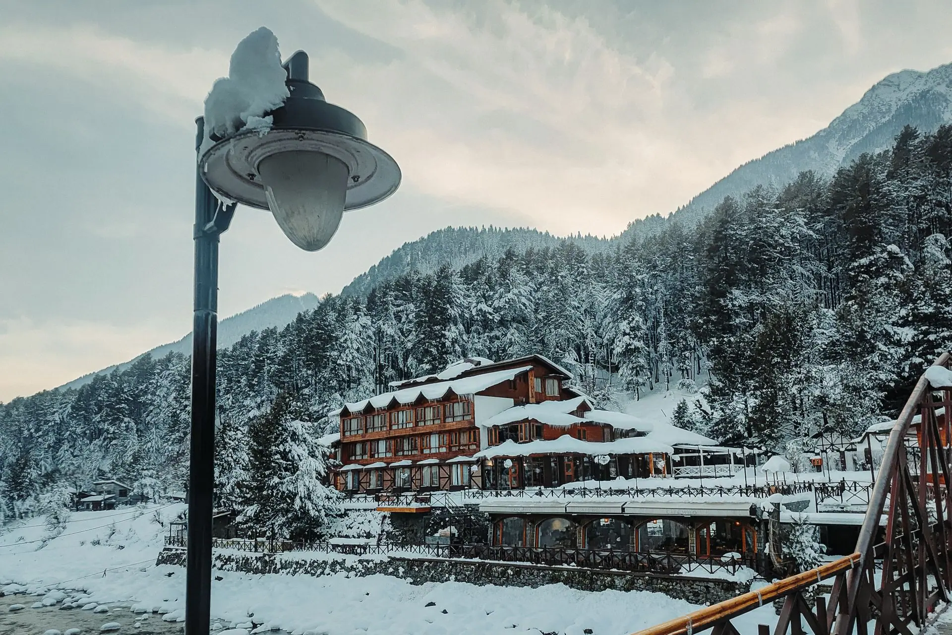 A snow-covered landscape in Pahalgam featuring a rustic building and snow-laden trees