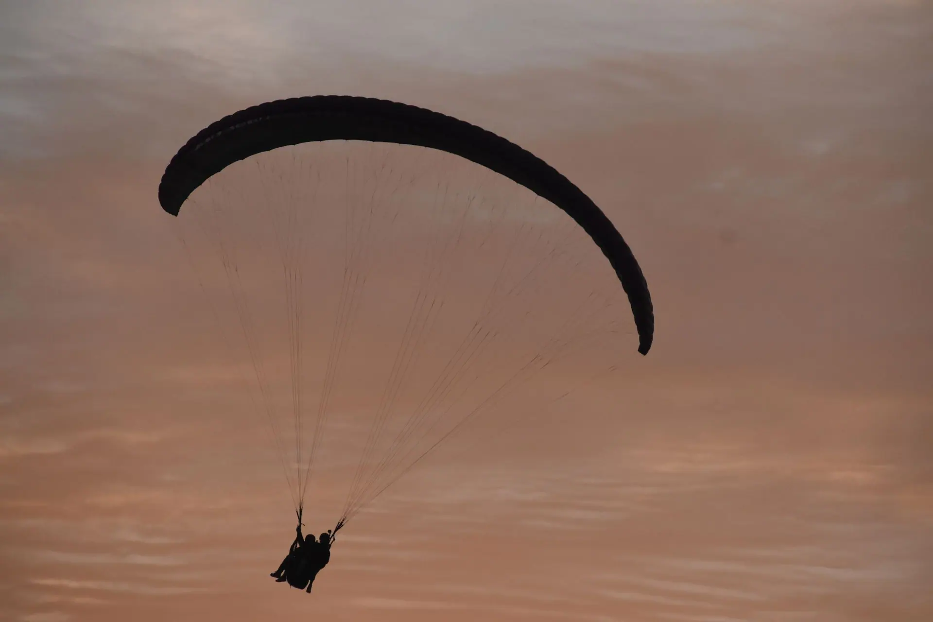 Silhouette of paragliders against a pink sunset sky in Bir, India