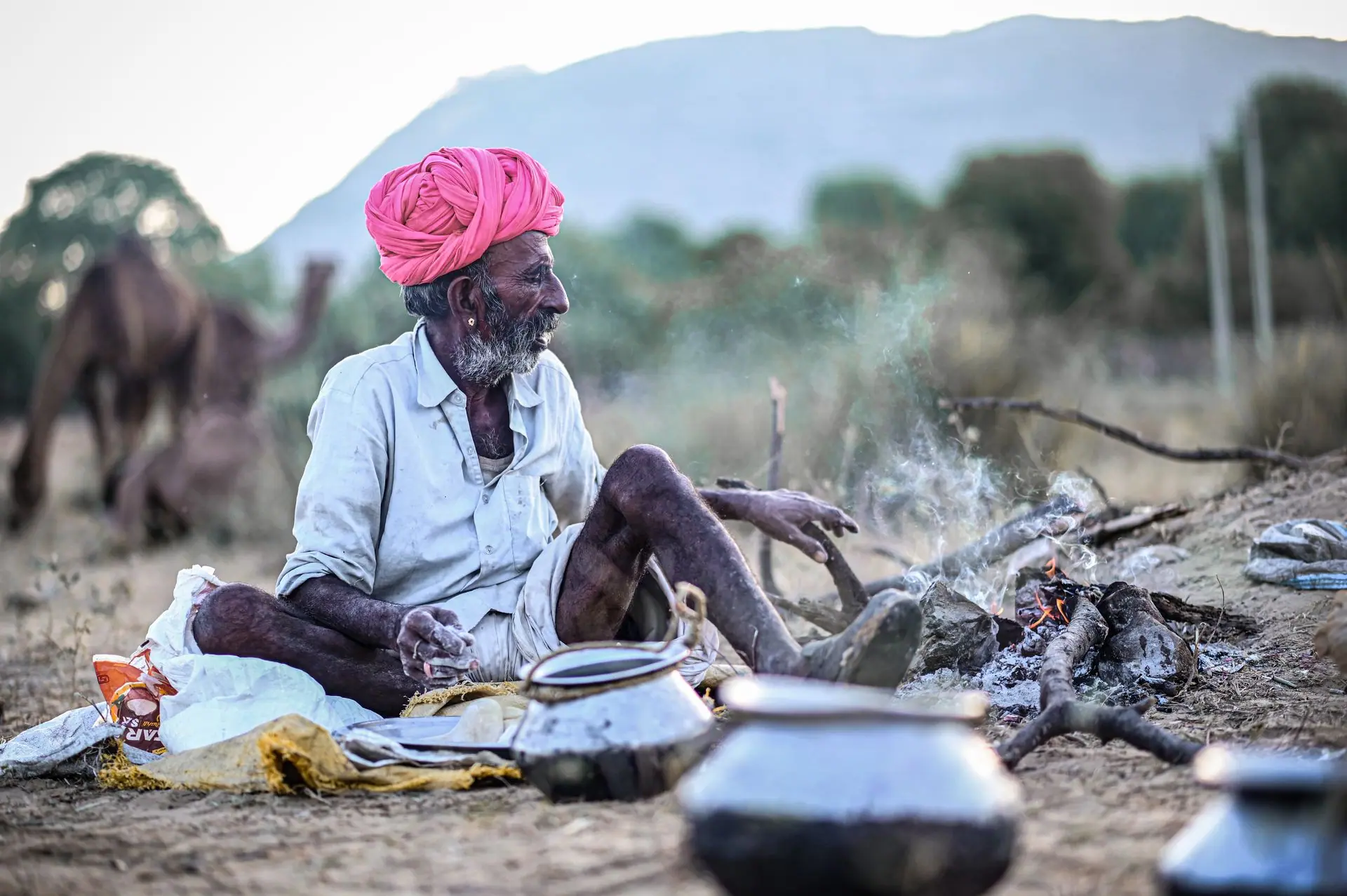 An elderly Indian man in a turban sitting by a bonfire in rural Pushkar, Rajasthan