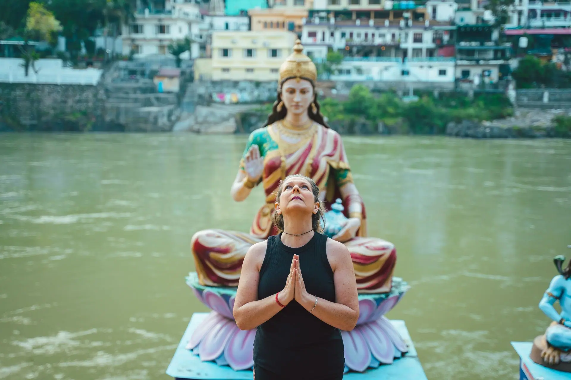 A woman praying beside a Hindu goddess statue by a river in Rishikesh, India