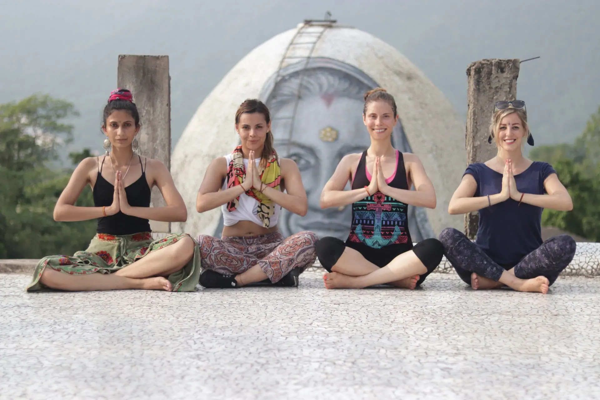 Four women practicing yoga with hands together at an outdoor class in Rishikesh, India