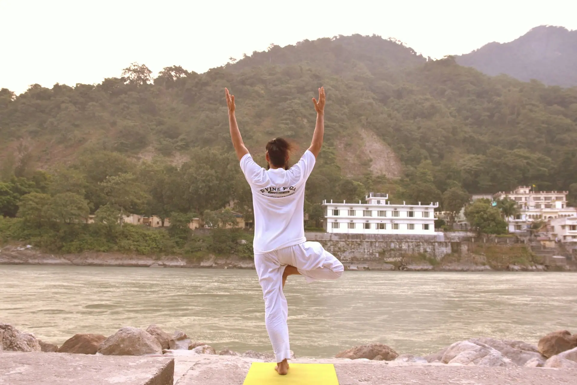 Back view of a man in a yoga pose by the Ganges River, Rishikesh, India, amidst serene nature