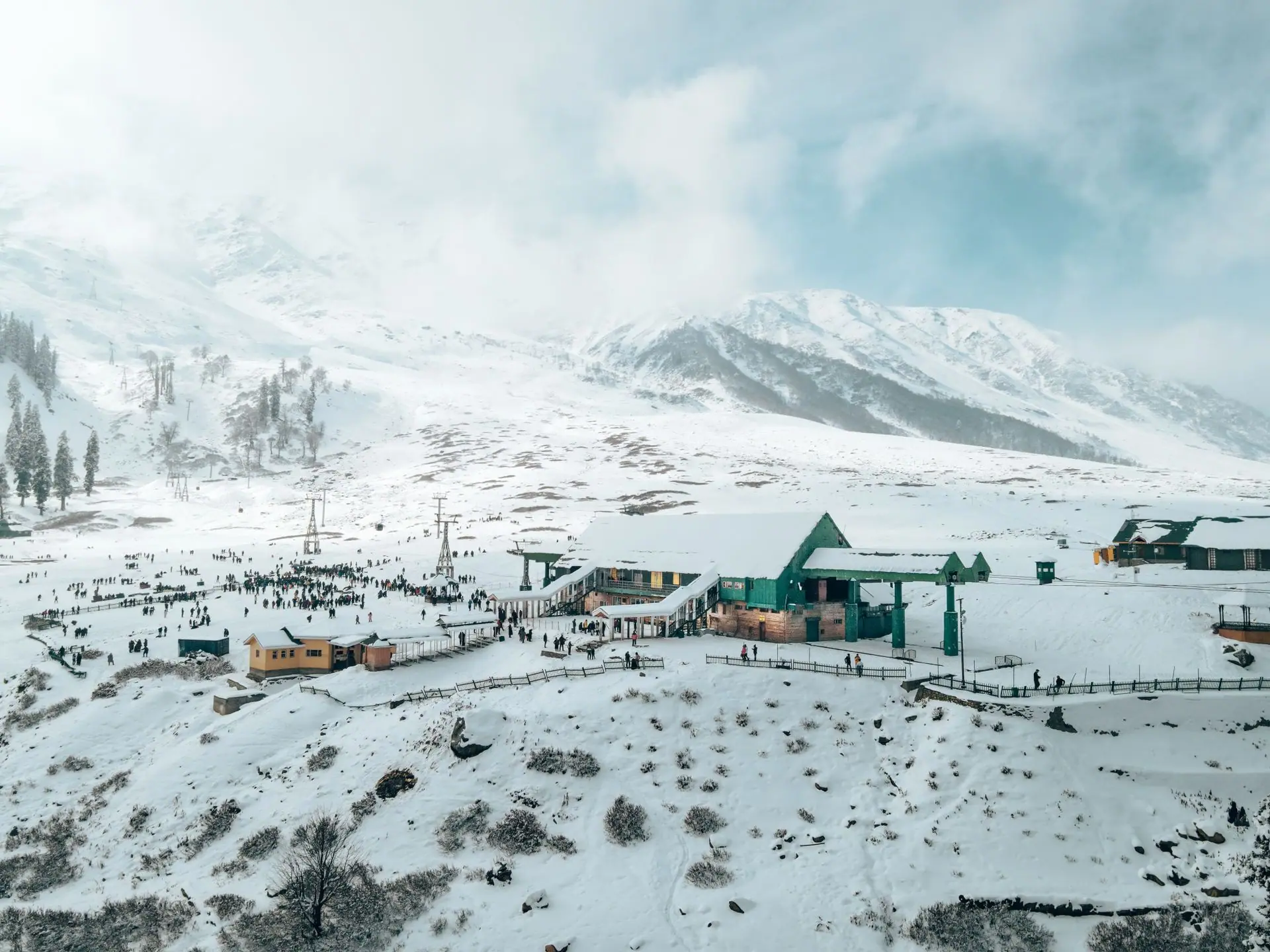Aerial view of Gulmarg ski resort with snowy mountains, vibrant buildings, and people enjoying winter activities