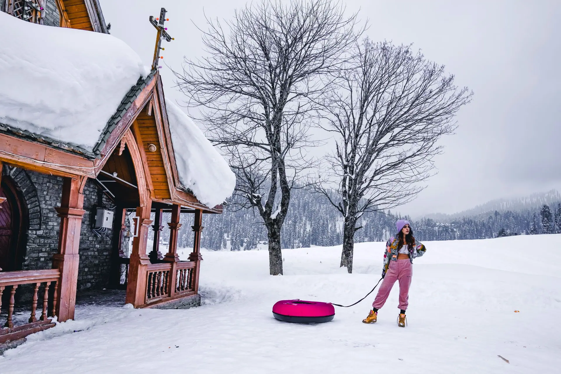 Woman enjoying winter snow in Gulmarg near a wooden cabin, perfect for winter adventure travel