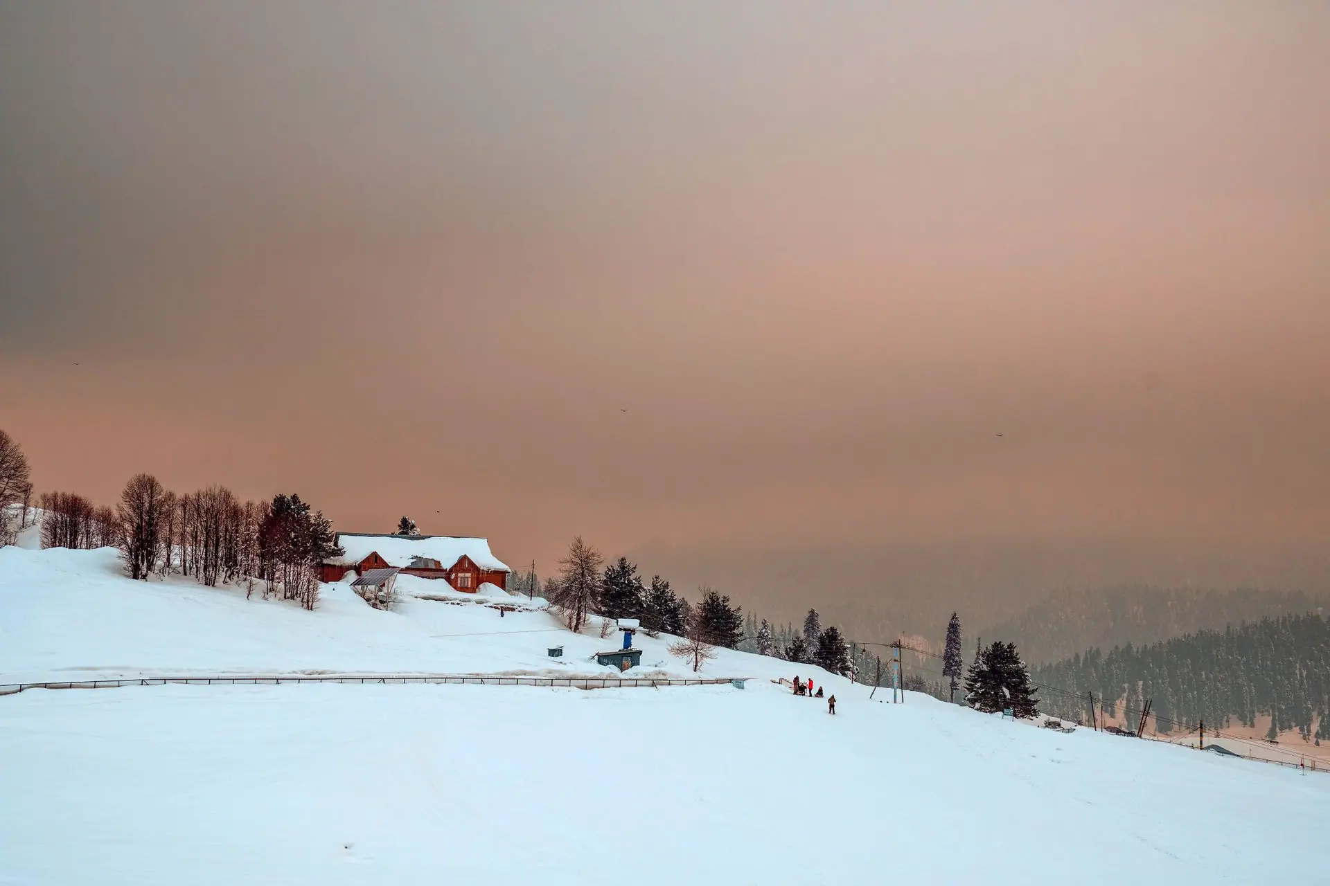 Capture of a serene winter landscape with snow-covered hills and a house at sunset in Gulmarg