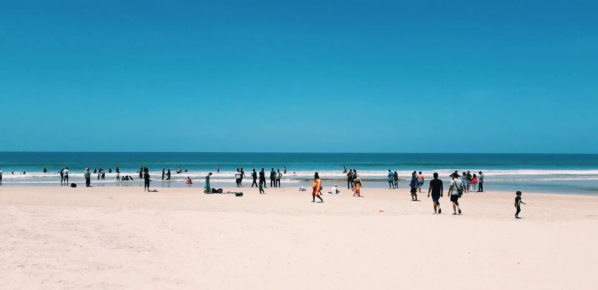 People enjoying a sunny day at Colva Beach in Goa, India, with clear blue skies and sandy shores