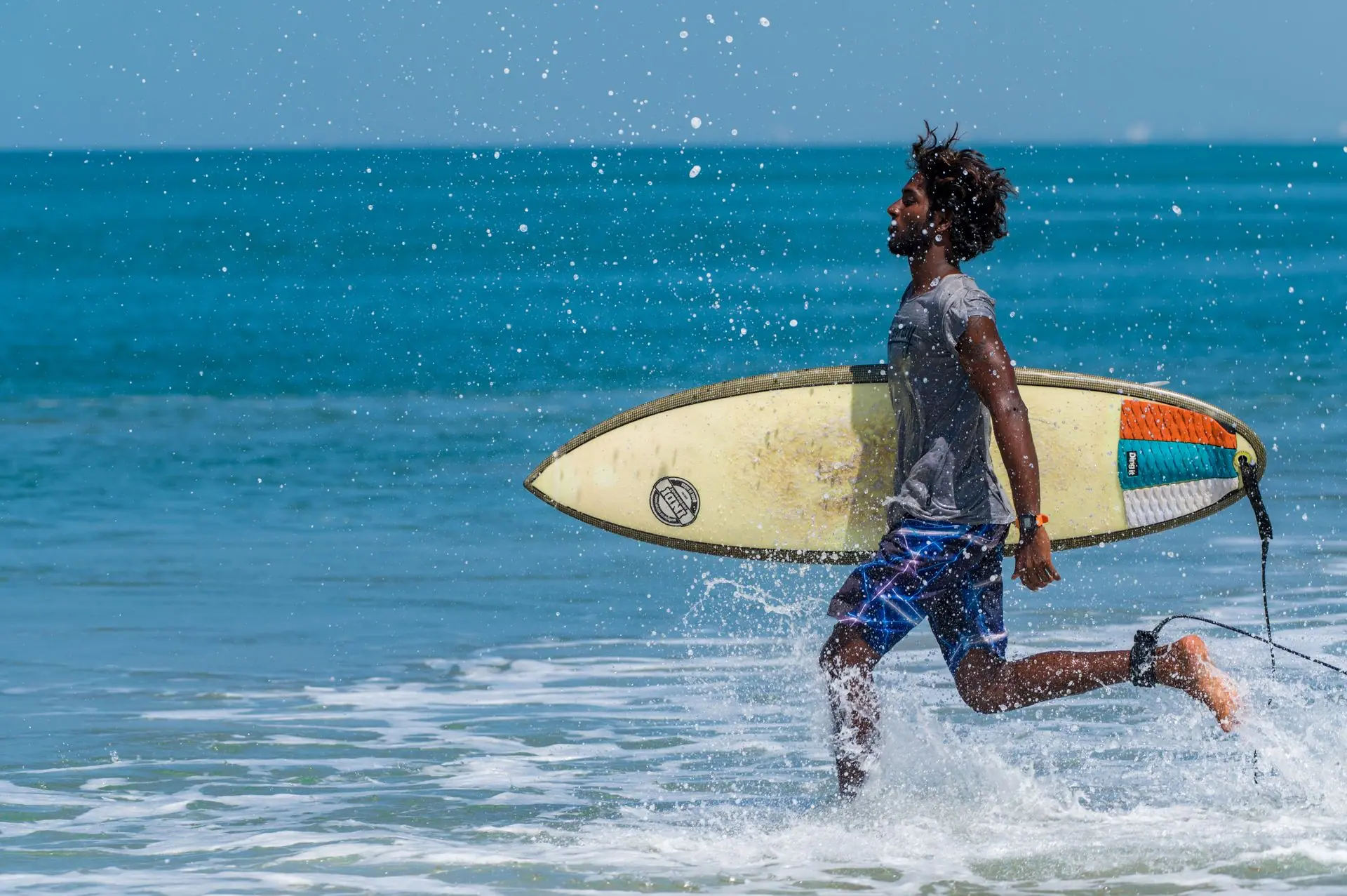 A young man runs with a surfboard along Varkala Beach in India, splashing through the ocean waves