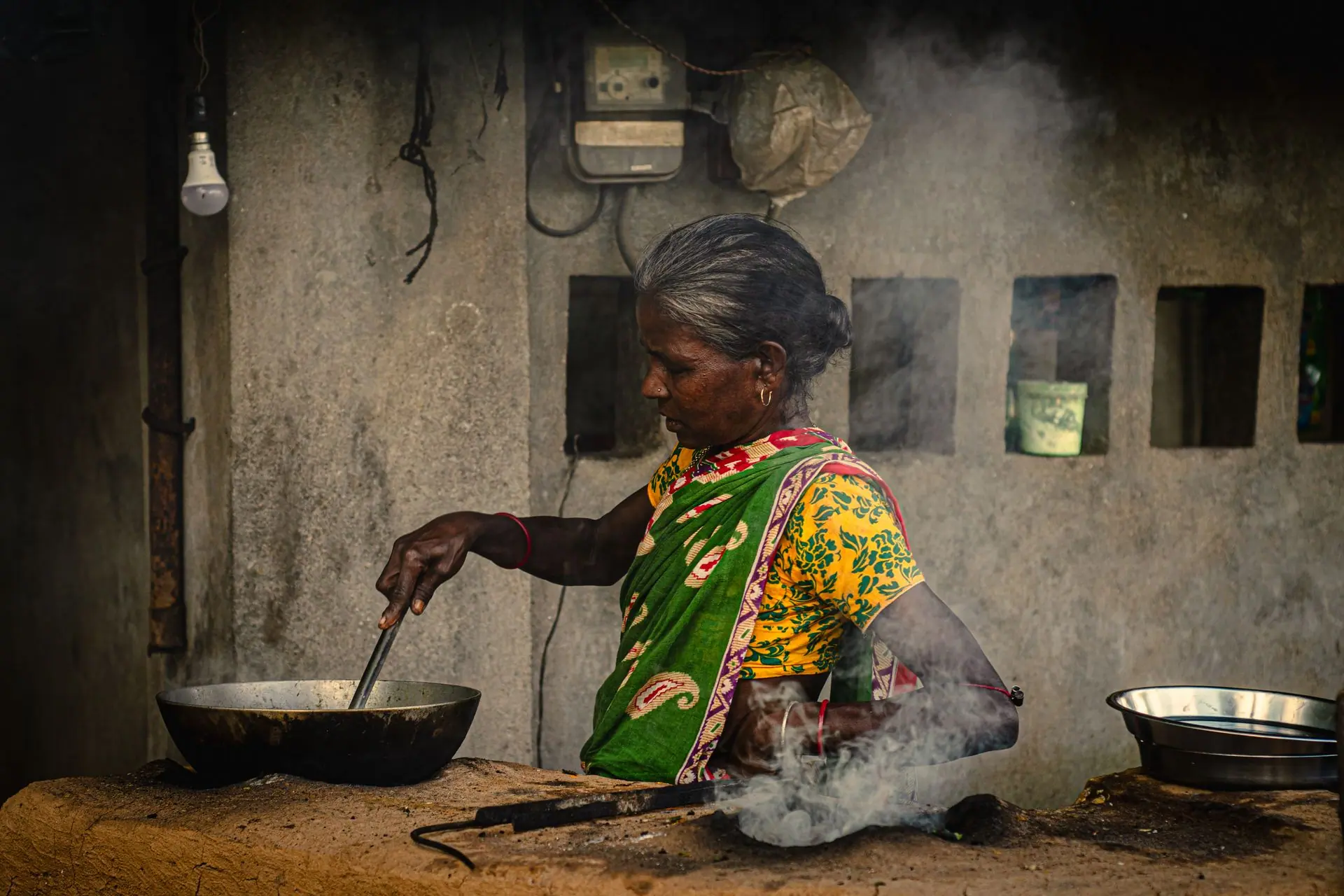A rural Indian woman in vibrant clothing prepares food outdoors using traditional methods