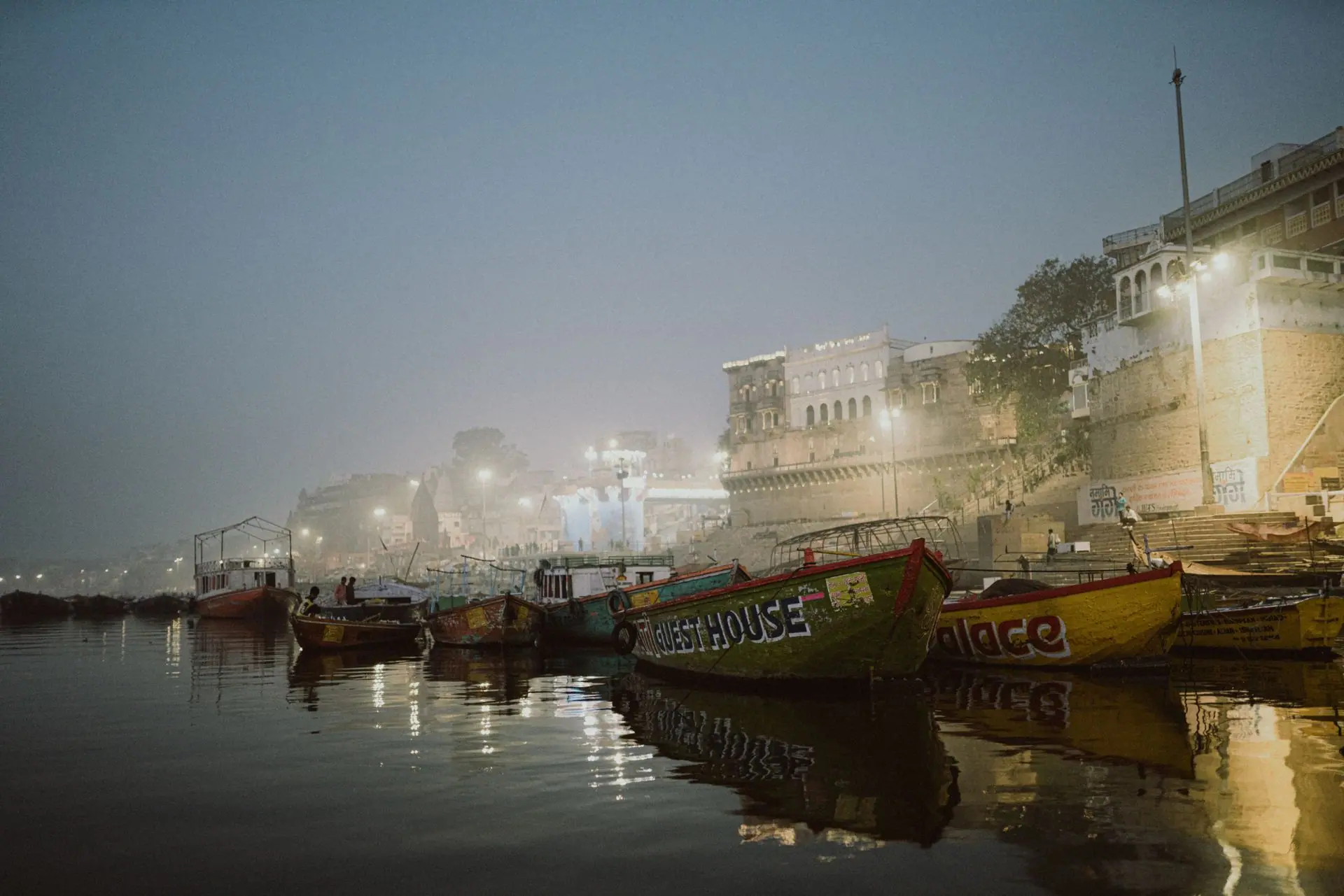 Misty evening view at Varanasi Ghats with colorful boats and illuminated buildings